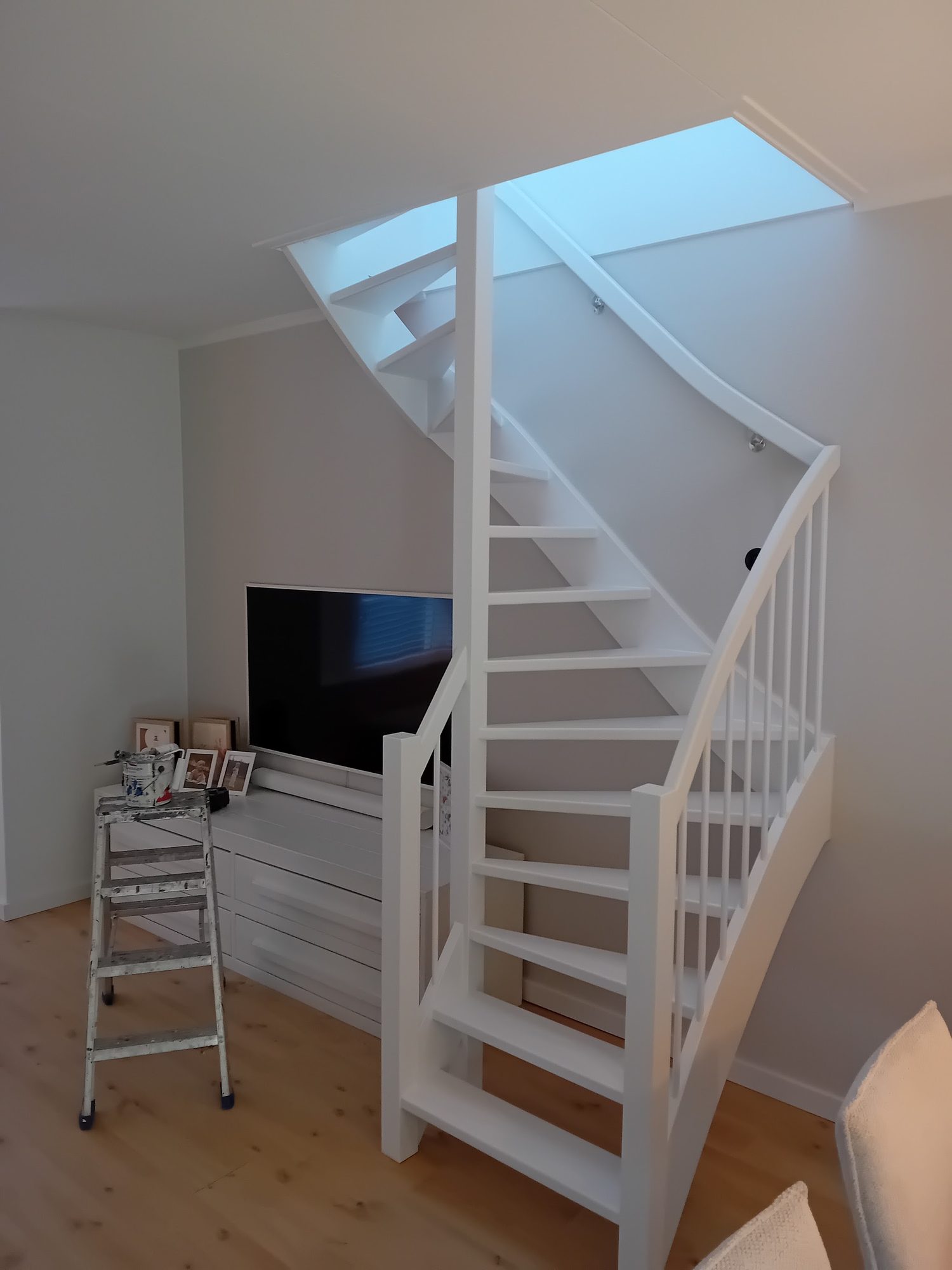 Witgeschilderde open trap met witte balustrade onder een dakraam
