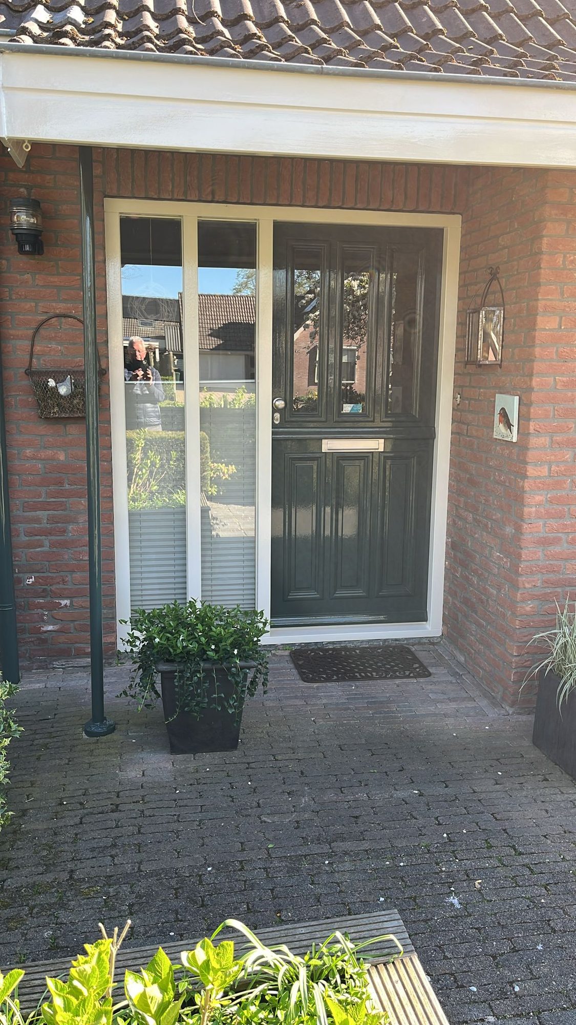 Portiek met donkere voordeur met glas, witte kozijnen en planten in potten