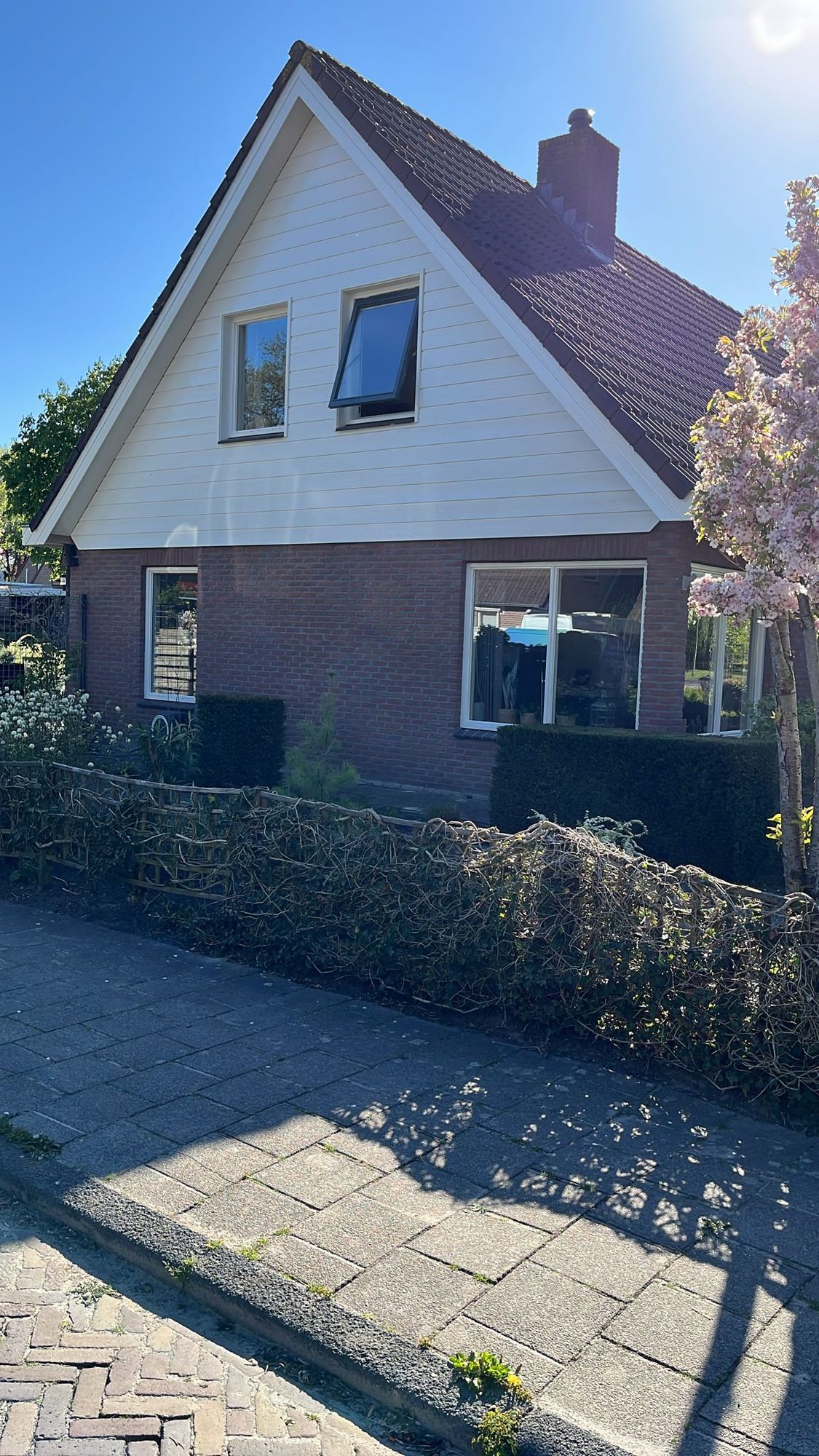 Vrijstaand huis met witgeschilderde houten topgevel en donkere kozijnen