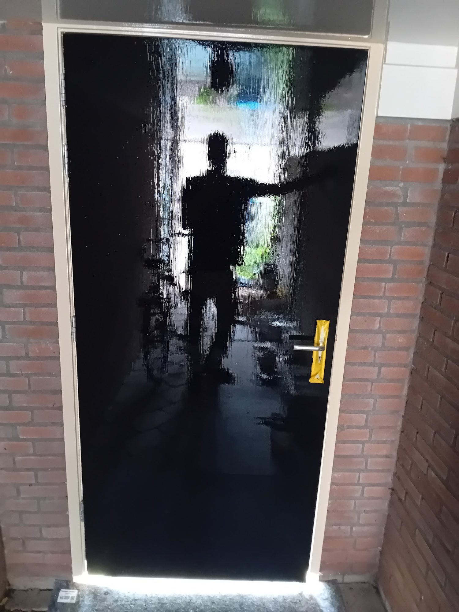 Zwarte voordeur in hoogglans die de straat weerspiegelt
